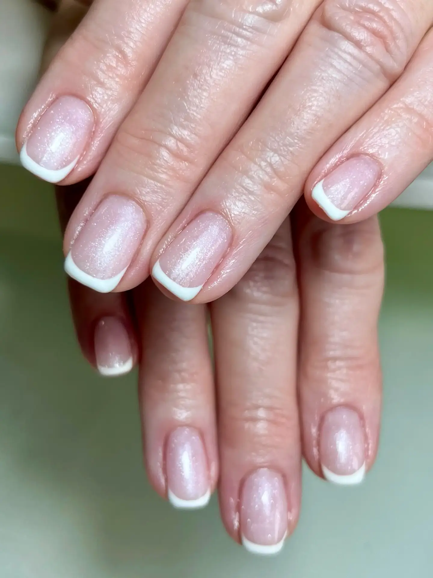 Close-up of hands with neatly manicured nails featuring a classic French tip design; the nails have a soft pink base and white tips, displaying a clean and elegant look.