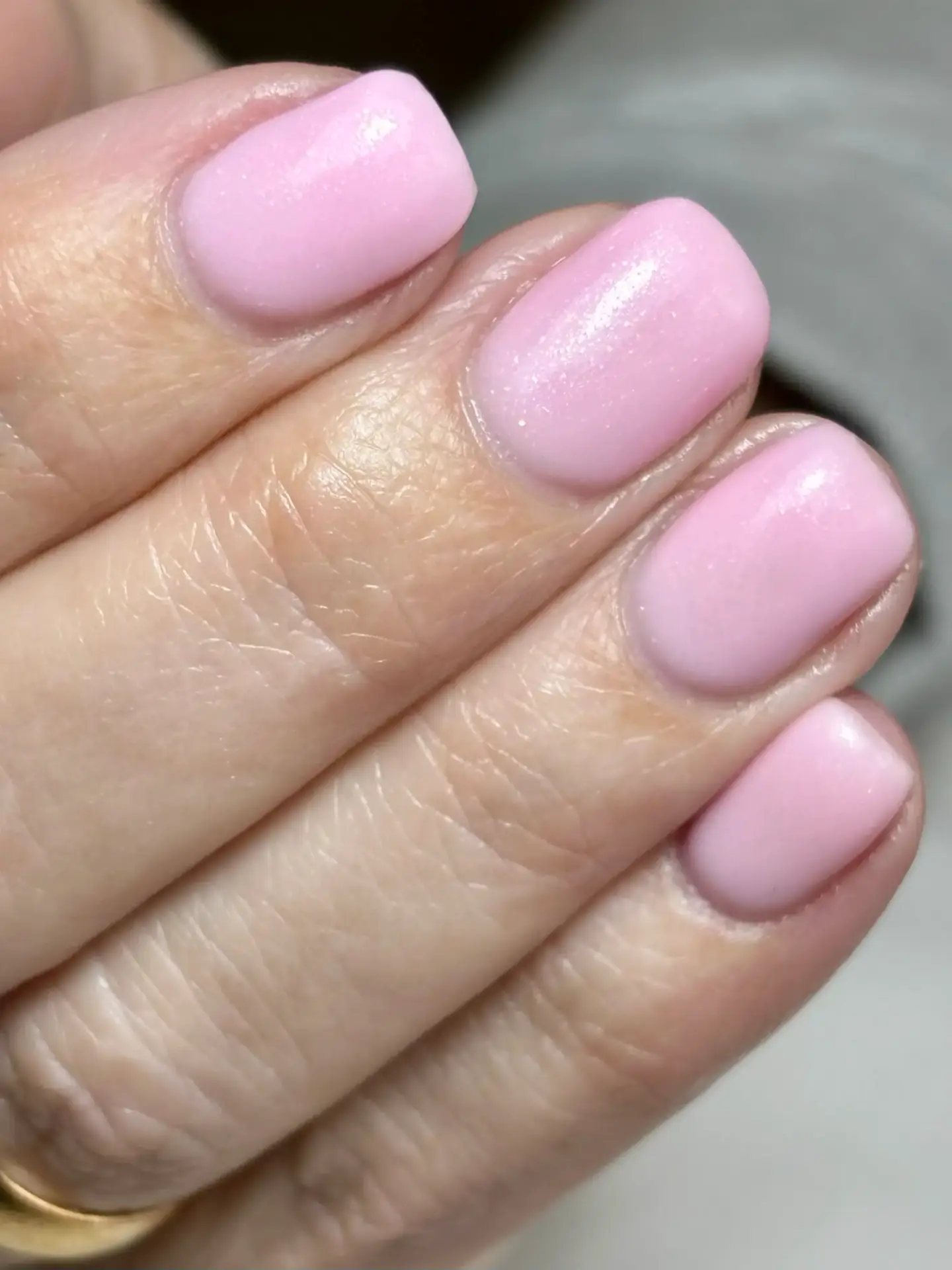 A close-up of a hand with short, neatly manicured nails painted in a glossy, pale pink colour. The skin appears smooth and the nails have a soft, natural shape.