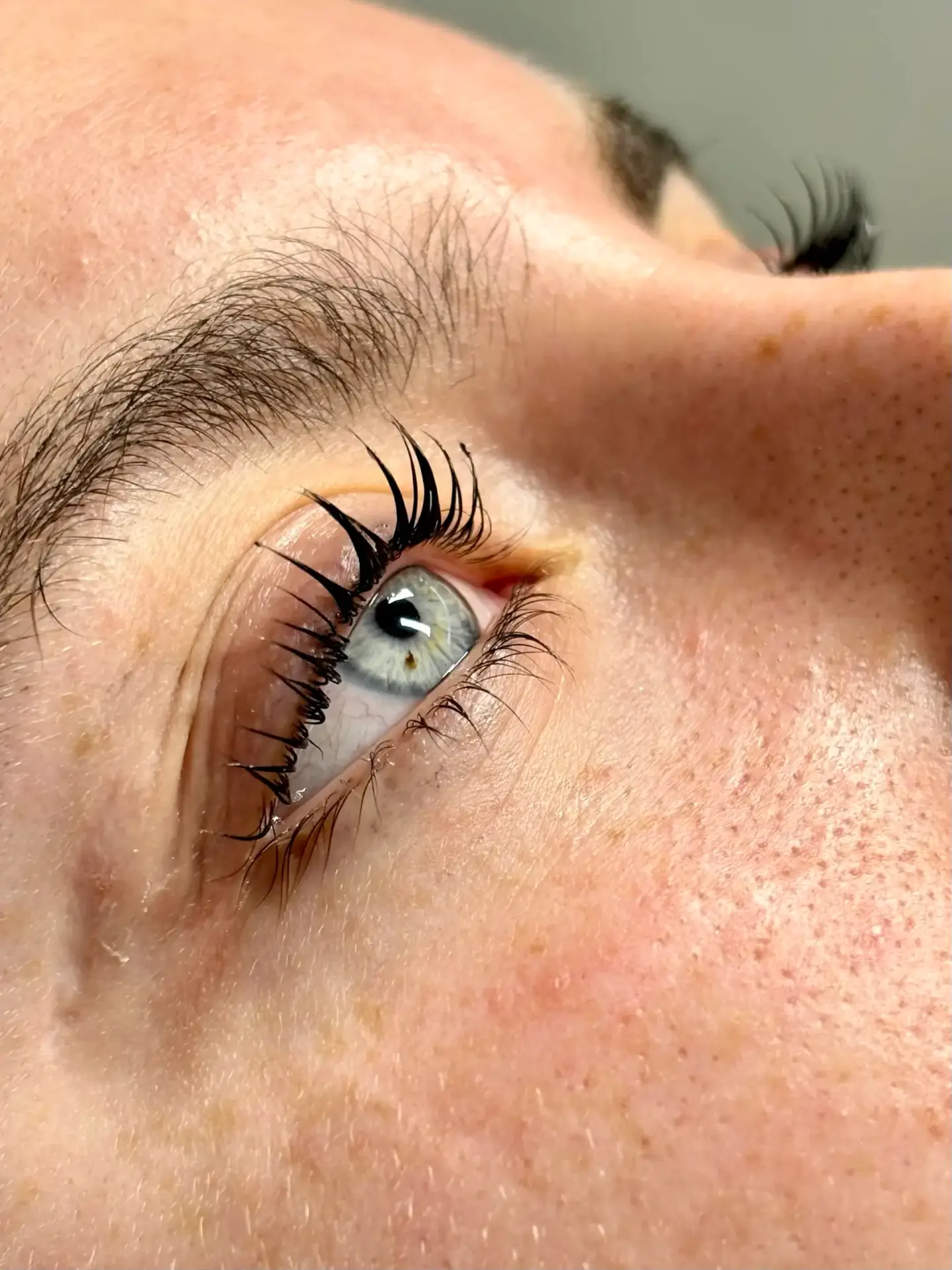 Close-up side view of a person's blue eye with long, curled eyelashes and visible skin texture, looking slightly upwards.