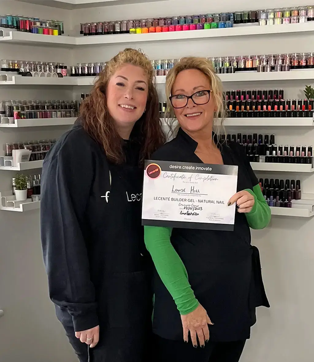 Two women smiling in a nail salon, holding a Lecenté Certificate of Completion for Louise Hills Builder Gel Natural Nail Conversion Course, dated 24/01/2023, surrounded by shelves of nail products.