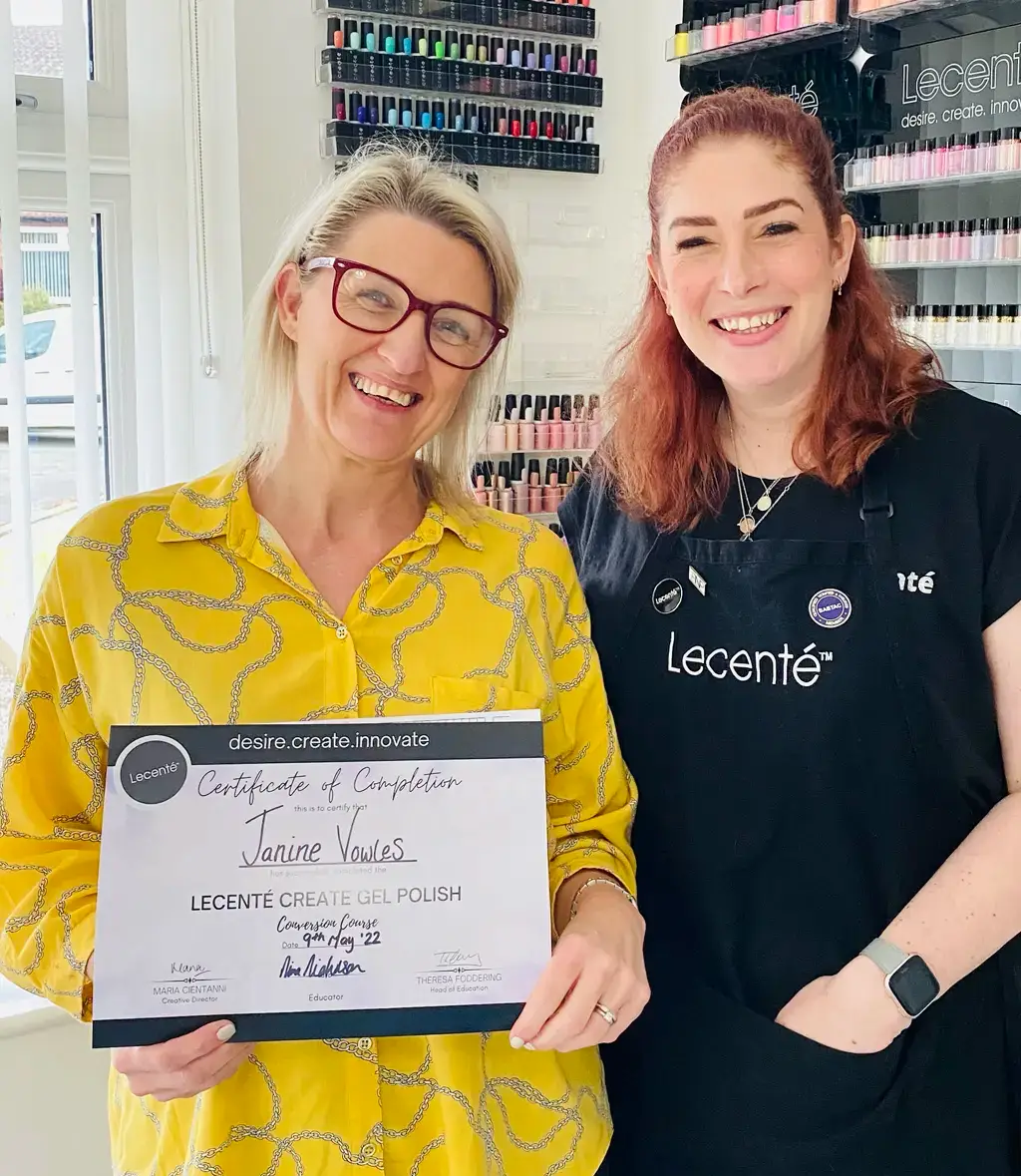 Two women smile in a nail salon. The woman on the left holds a certificate of completion for a Lecenté gel polish course. Nail varnish bottles are displayed on shelves behind them.